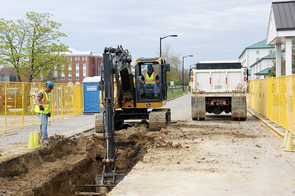 Excavadora y operario instalando una tubería de agua en una zanja