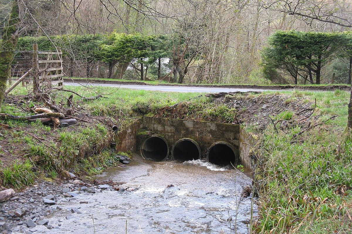 Tres alcantarillas de tubo bajo una vía que desaguan en una quebrada