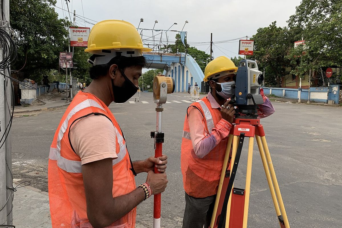 Topógrafos con casco y chaleco operando una estación total en una calle